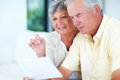 Buy stock photo Happy, mature couple and reading with bills for finance, expenses or budget planning on sofa at home. Elderly, man and woman with smile for pension fund, mortgage or financial payments at house