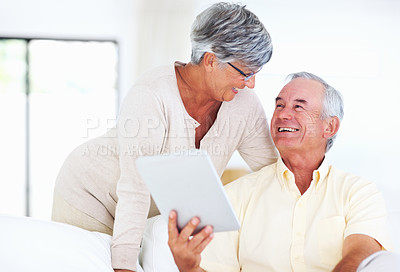 Buy stock photo Cheerful mature couple smiling while using tablet PC at home