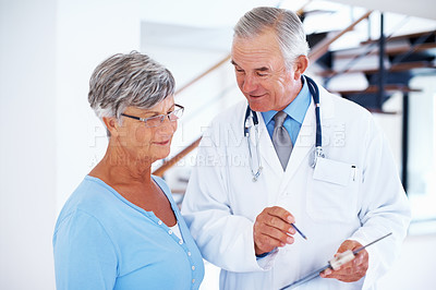 Buy stock photo Handsome mature doctor discussing report with patient in hospital
