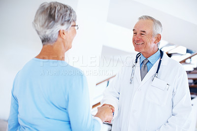 Buy stock photo Smiling mature doctor shaking hands with woman in hospital