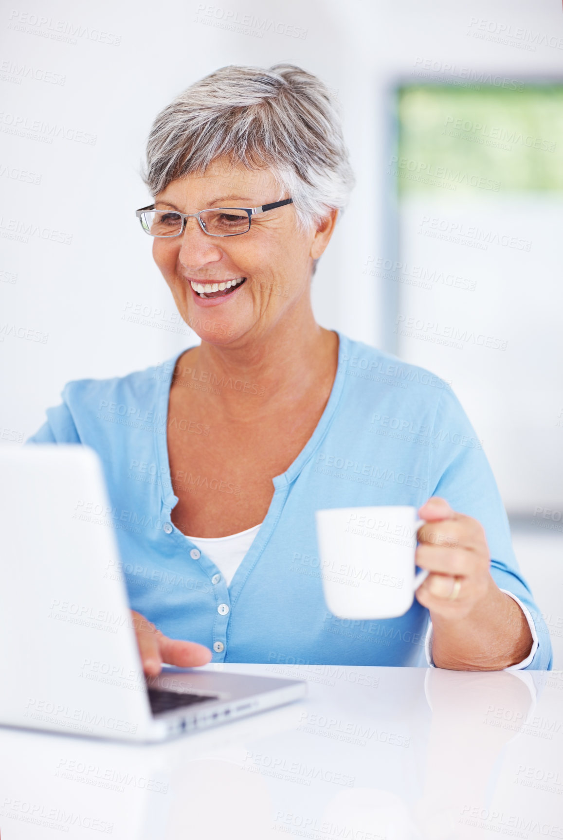Buy stock photo Happy mature woman using laptop while enjoying coffee at home