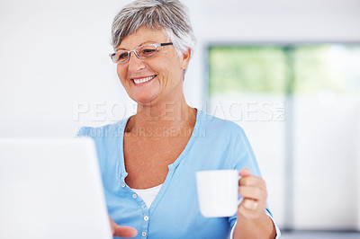 Buy stock photo Smiling mature woman using laptop while enjoying coffee at home