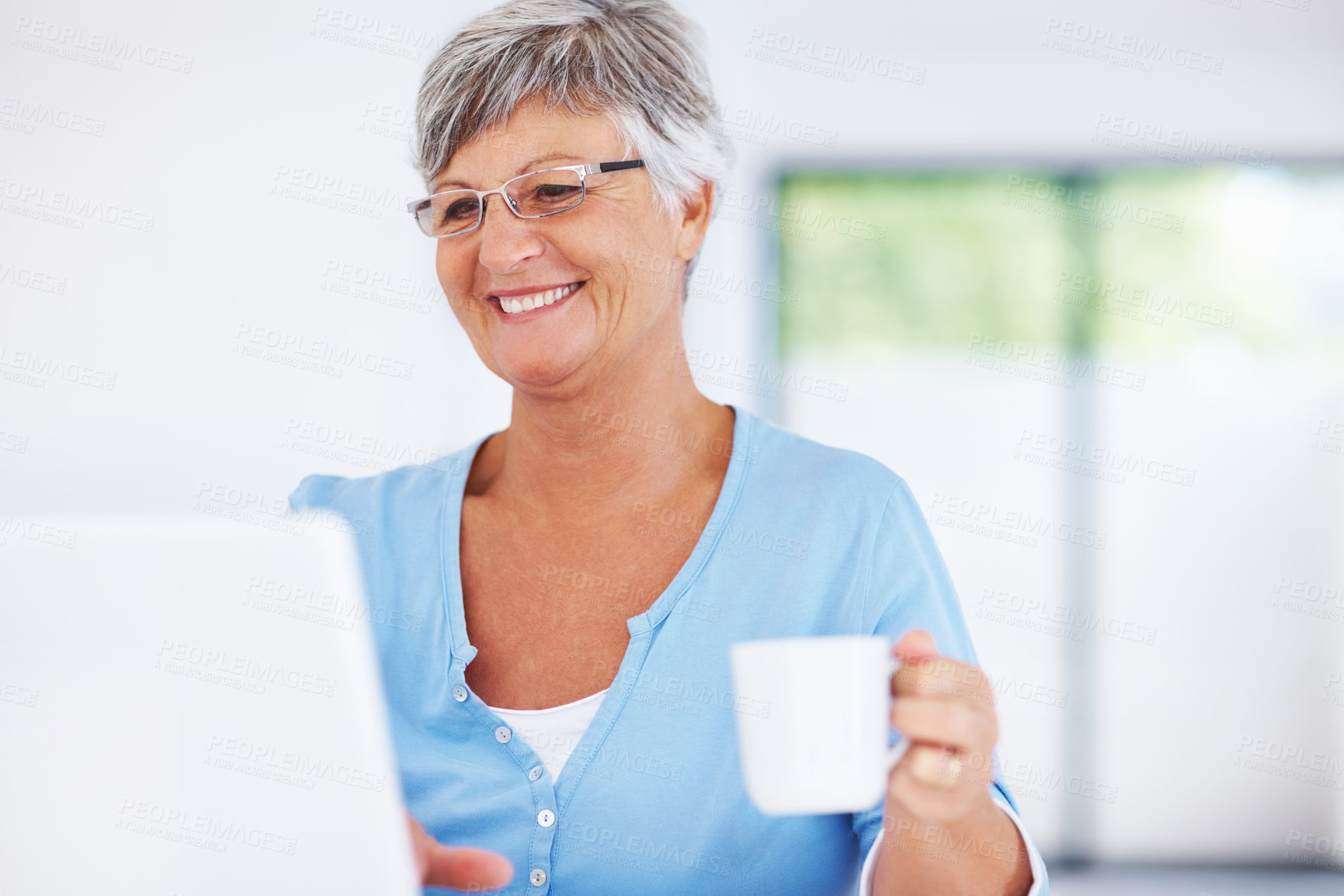 Buy stock photo Smiling mature woman using laptop while enjoying coffee at home