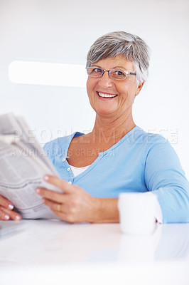 Buy stock photo Smiling mature woman reading newspaper while enjoying morning cup of coffee