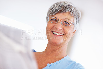 Buy stock photo Closeup of happy mature woman with glasses smiling while reading newspaper
