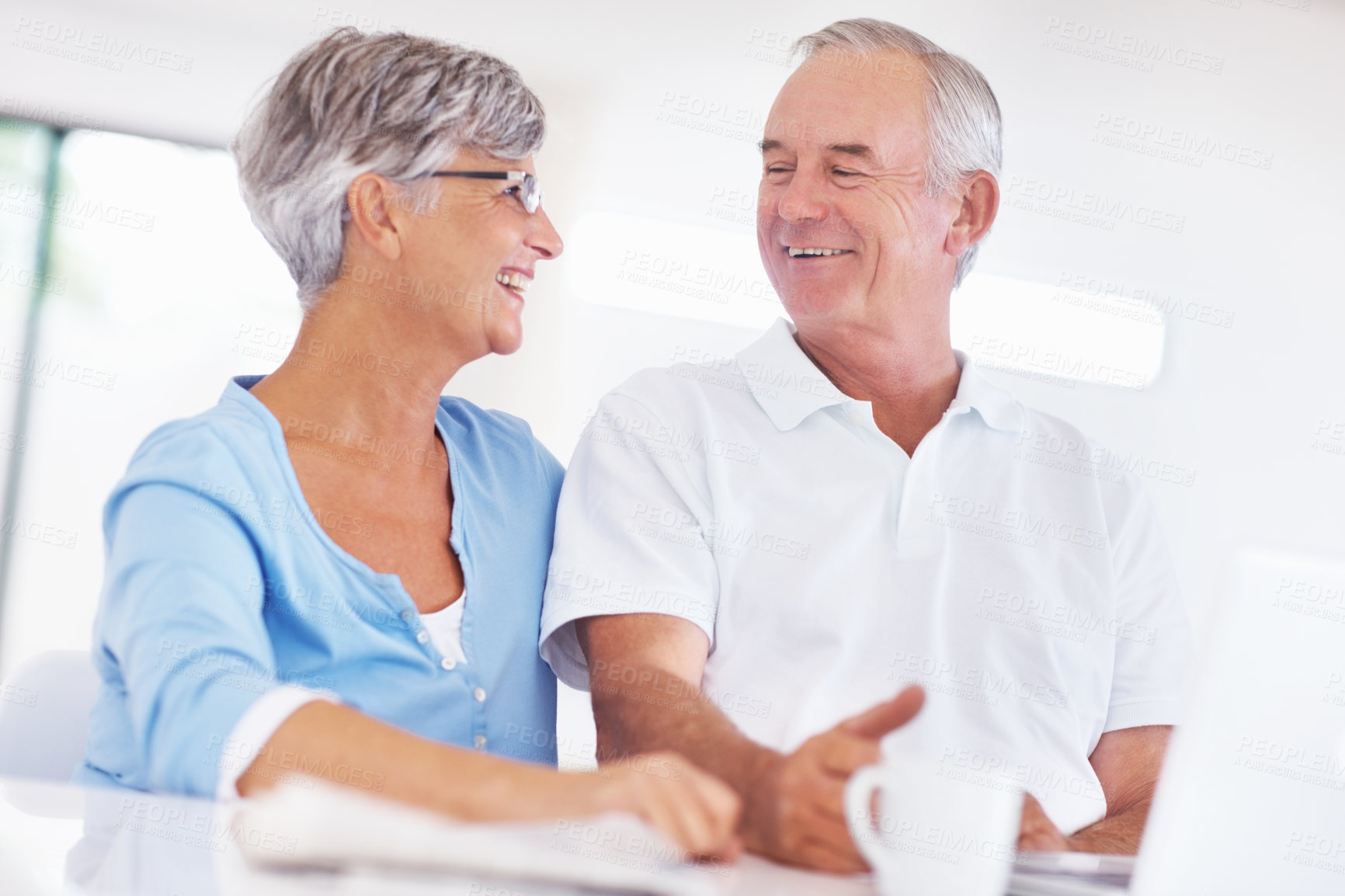 Buy stock photo Happy mature couple looking at each other while using laptop at home