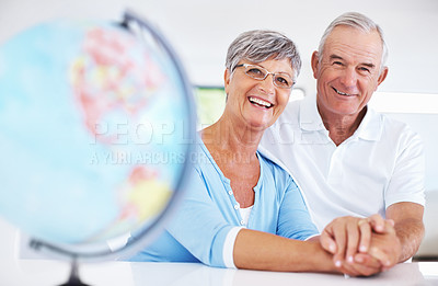 Buy stock photo Happy mature couple smiling while holding hands at the table with globe