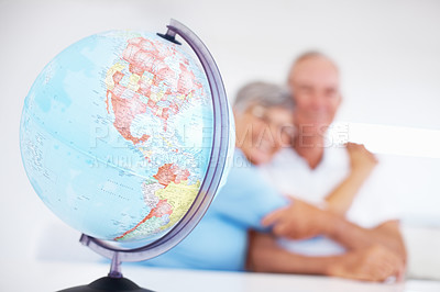 Buy stock photo Focus on globe placed on table with smiling mature couple embracing in background