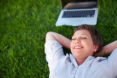 Buy stock photo Relaxed mature woman with laptop smiling while lying on grass