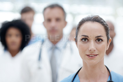Buy stock photo Young female doctor looking at the camera with her colleagues in the background