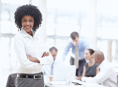 Buy stock photo An african woman standing confidently in the office with her colleagues in the background