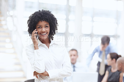 Buy stock photo An african woman speaking on her cellphone in the office with her colleagues behind her