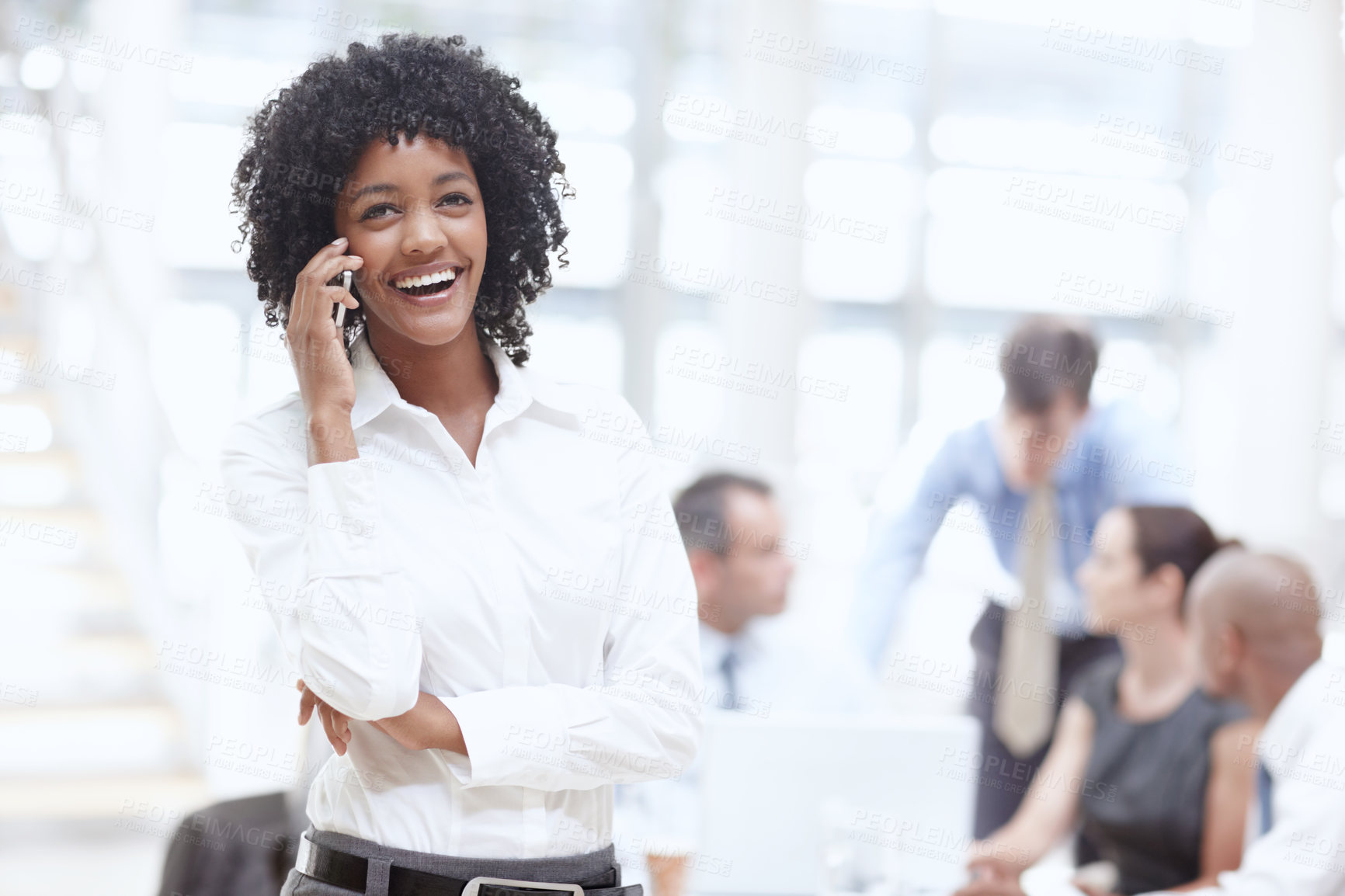 Buy stock photo An african woman talking on her cellphone in the office with her colleagues behind her