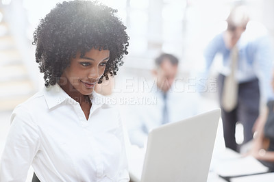 Buy stock photo An african woman working on her laptop in the office with her colleagues behind her