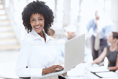 Buy stock photo An african woman holding a laptop in the office with her colleagues in the background