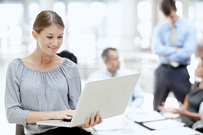 Buy stock photo A beautiful young woman using her laptop in the office with her colleagues behind her