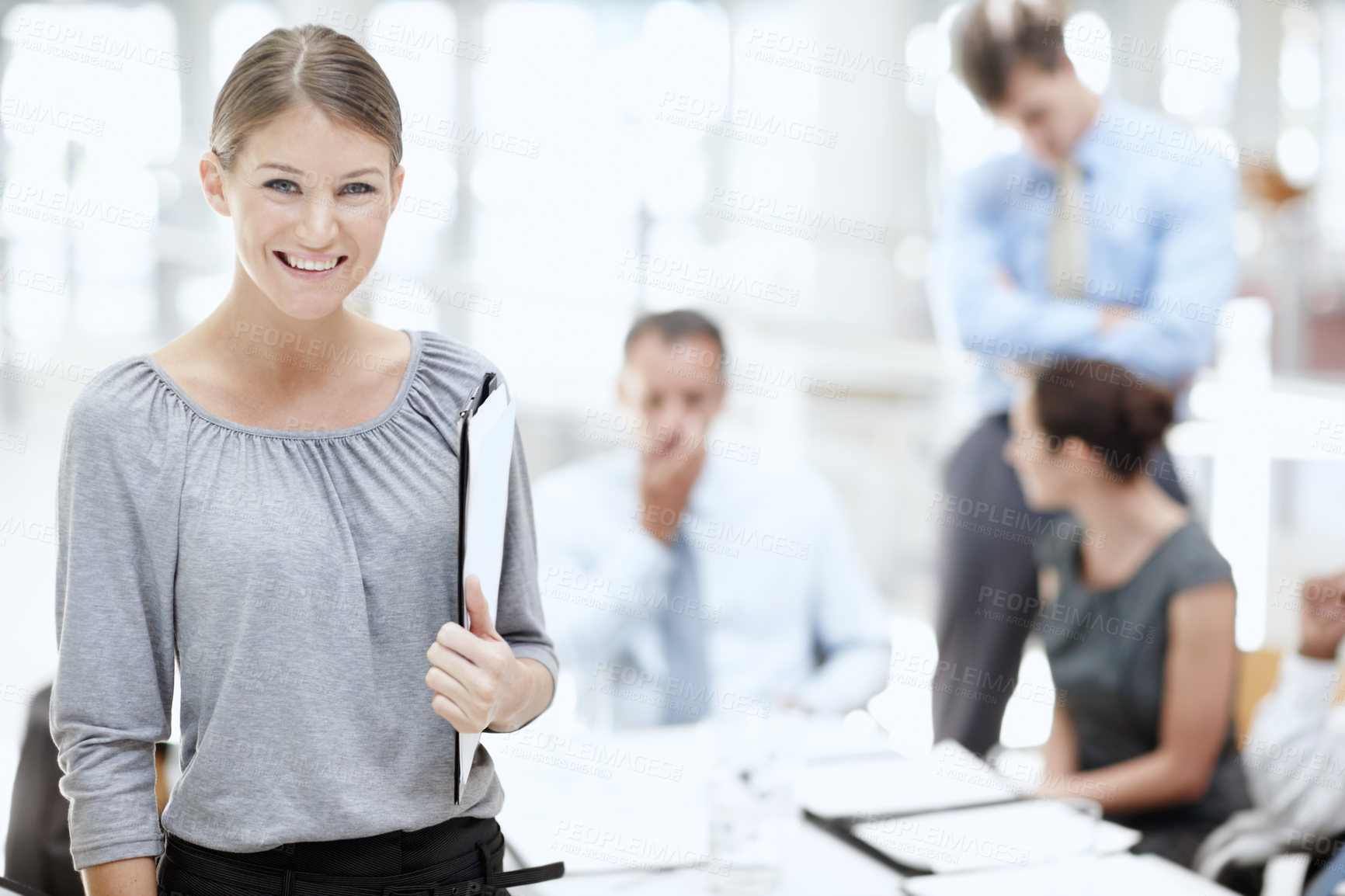 Buy stock photo A young woman standing with a notebook in the office with her colleagues behind her