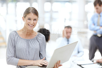 Buy stock photo An attractive young woman using her laptop in the office with her colleagues behind her