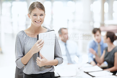 Buy stock photo A young woman holding her notebook in the office with her colleagues in the background