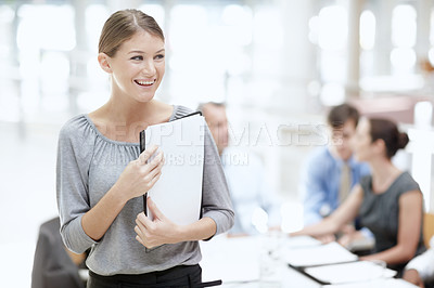 Buy stock photo An attractive woman standing with a notebook in the office with her colleagues behind her