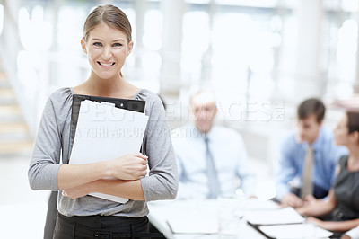 Buy stock photo A young woman with a notebook standing in the office with her colleagues behind her