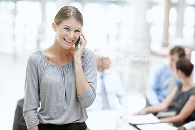 Buy stock photo A young woman using her cellphone in the office with her colleagues in the background