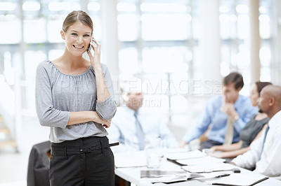 Buy stock photo An attractive woman using her cellphone in the office with her colleagues in the background