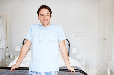 Buy stock photo A man standing by his bed dressed in comfortable pajamas or lounge wear and looking away. A young brunette male relaxing in his modern bright bedroom at home on the weekend