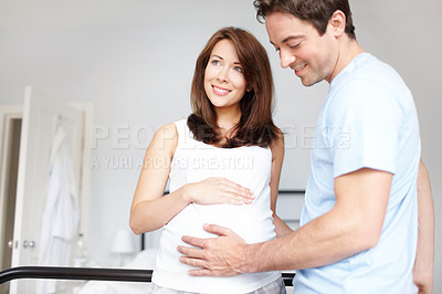 Buy stock photo Young man touching his pregnant wifes stomach while at home as she looks on