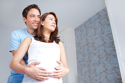 Buy stock photo Young man holding his girlfriends pregnant belly as they look on in thought