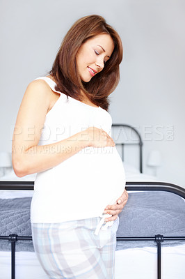 Buy stock photo Happy young woman standing in her bedrooom while she holds her pregnant belly