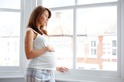 Buy stock photo Pretty young pregnant woman looking out her bedroom window as she holds her belly