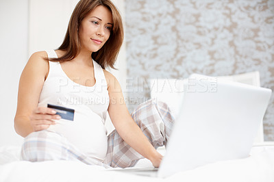 Buy stock photo Pretty young pregnant woman sitting on her bed while using her credicard to buy something online