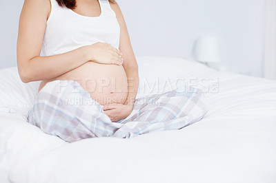 Buy stock photo Cropped image of a young woman holding her pregnant belly on her bed