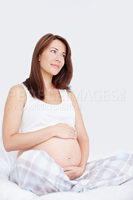 Buy stock photo Pretty young woman sitting on her bed holding her bare pregnant belly while looking away in thought