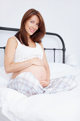 Buy stock photo Pretty young woman sitting on her bed holding her bare pregnant belly while looking at you