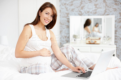 Buy stock photo Happy pregnant woman sitting on her bed while using her laptop