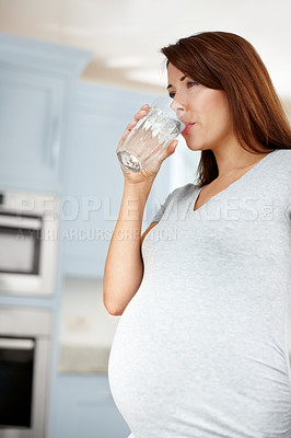 Buy stock photo Young pregnant woman drinking a glass of water in her kitchen