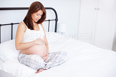 Buy stock photo A pregnant woman sitting on her bed and holding her exposed baby bump