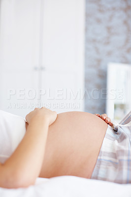 Buy stock photo Cropped closeup of a pregnant woman holding her baby bump while lying in bed - Copyspace