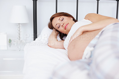 Buy stock photo A pregnant woman lying in bed and looking at her baby bump longingly - Copyspace