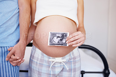 Buy stock photo An expectant couple holding hands while she places an ultrasound photo over her belly