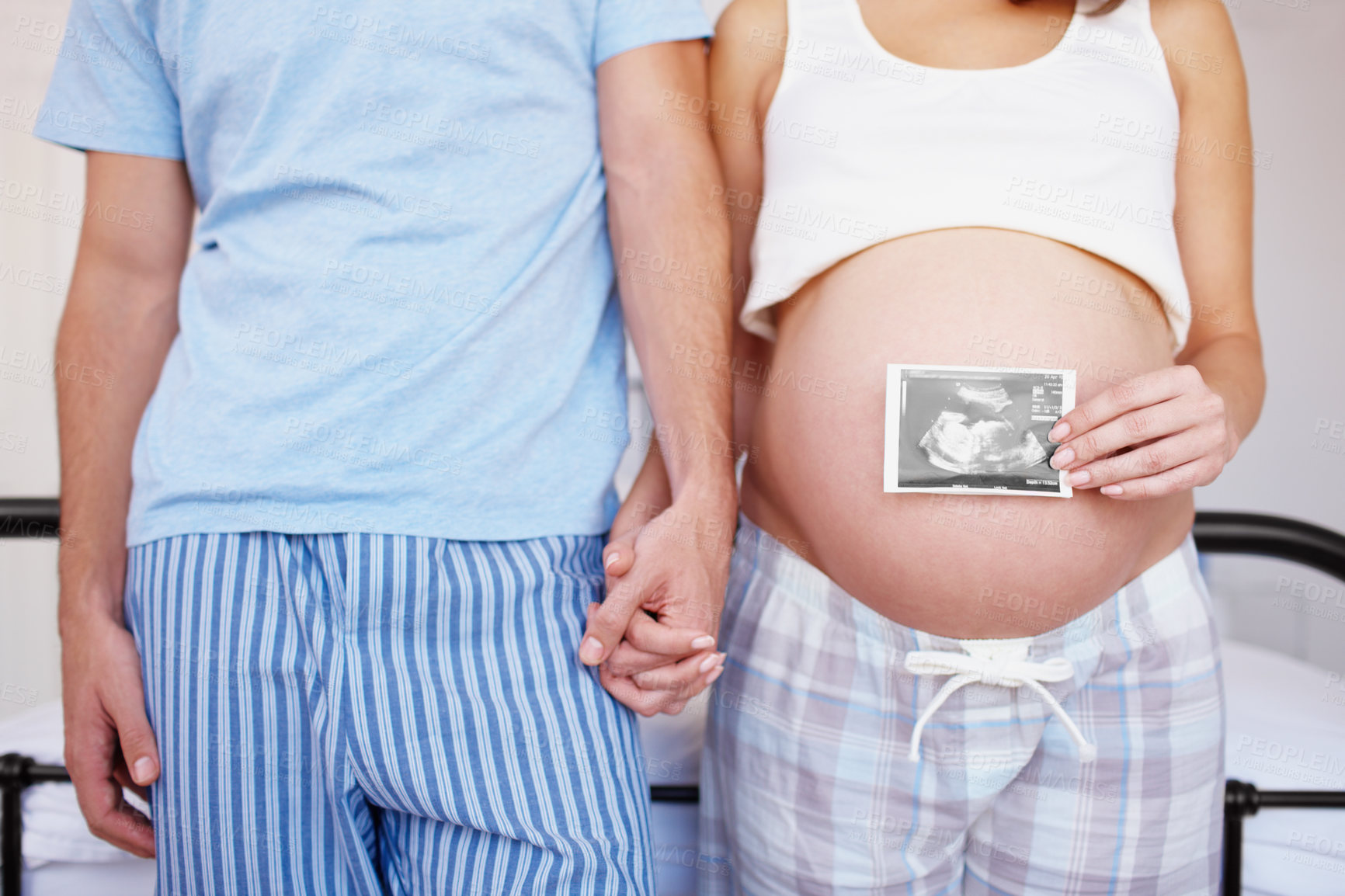 Buy stock photo An expectant couple holding hands while she places an ultrasound photo over her belly