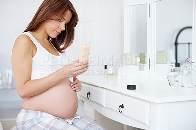 Buy stock photo A beautiful pregnant woman rubbing skin moisturiser on her baby bump in the bathroom