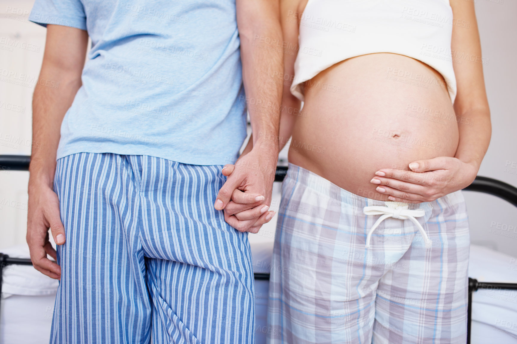 Buy stock photo Stomach, pregnant and couple with love, bedroom and care in home and affection for unborn baby. House, man and woman with belly, relationship and bonding for parenthood, holding hands and family