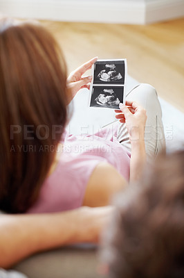 Buy stock photo Over the shoulder view of a young pregnant woman looking at her babies sonogram
