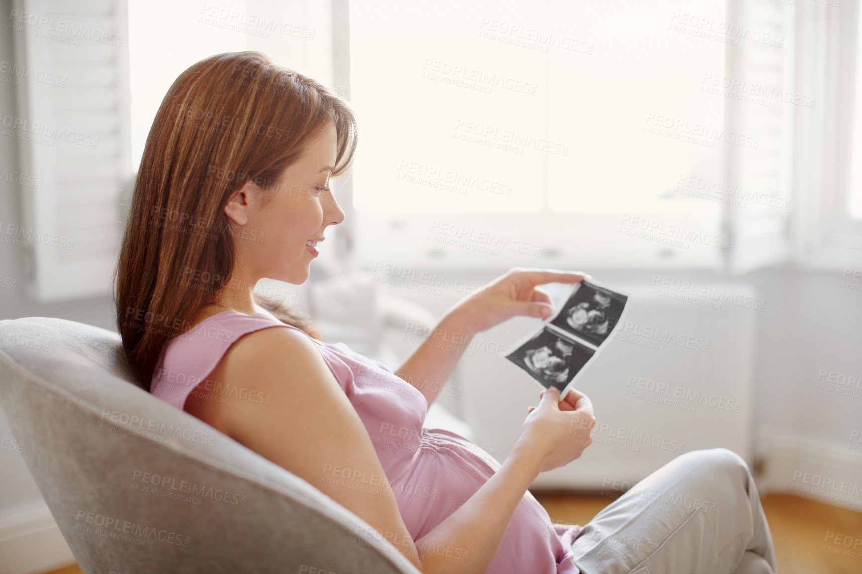 Buy stock photo Pretty young woman looking at her babies sonogram while sitting at home