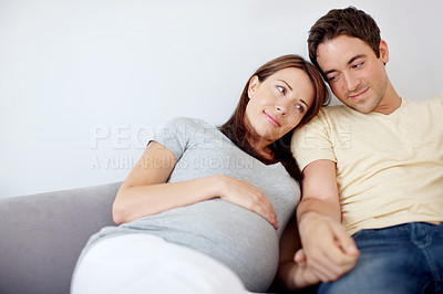 Buy stock photo Happy young pregnant couple sitting on their couch at home relaxing