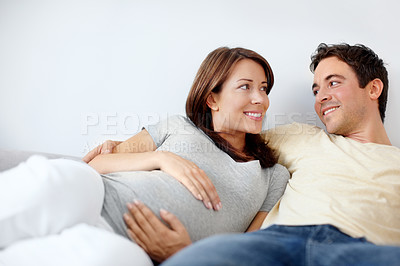 Buy stock photo Happy expecting couple sitting in their living room as they look at eachother
