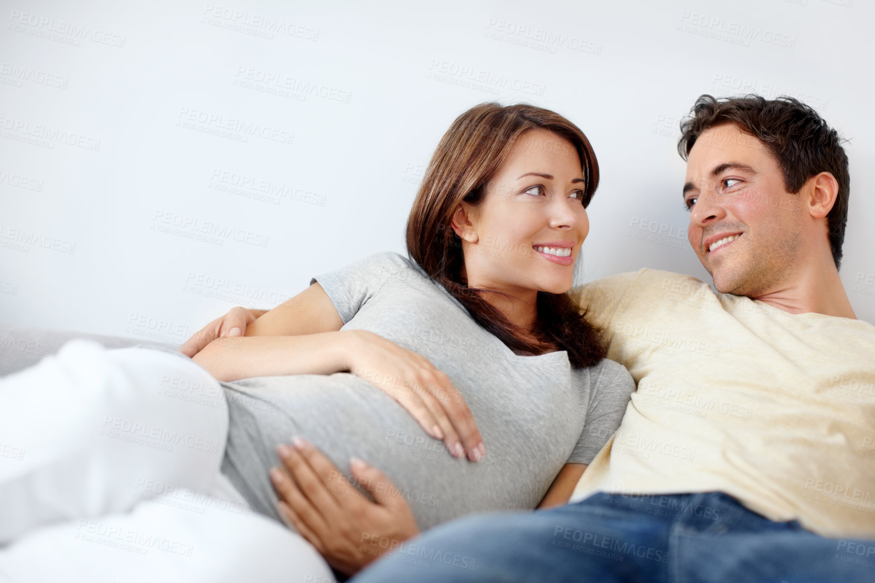 Buy stock photo Couple, apartment and smile for pregnancy on sofa in living room on maternity break, bonding or relax. People, love and happy in relationship at home for support, trust and care for future or growth